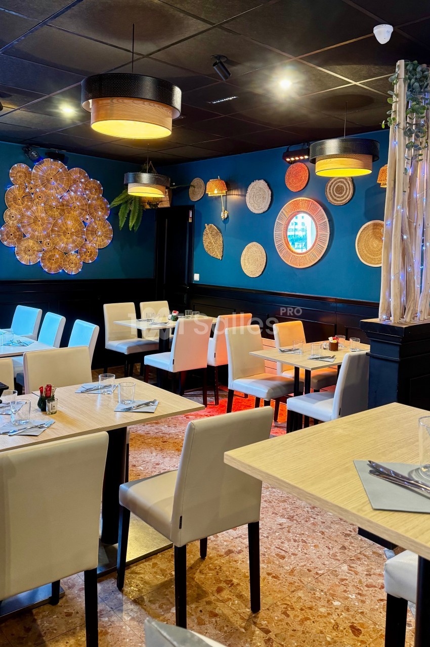 Salle de restaurant moderne avec tables dressées, chaises blanches, décoration murale et éclairage chaleureux.