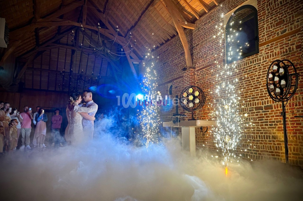 Un couple danse au milieu de la fumée et des étincelles dans une salle en briques avec un plafond en bois.