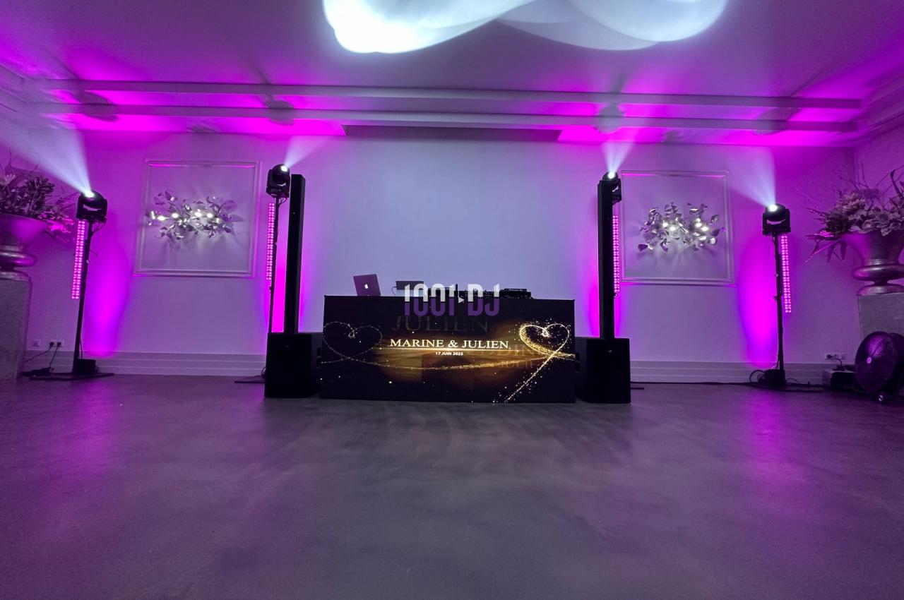 Console de DJ illuminée avec des projecteurs roses dans une salle décorée de fleurs blanches.