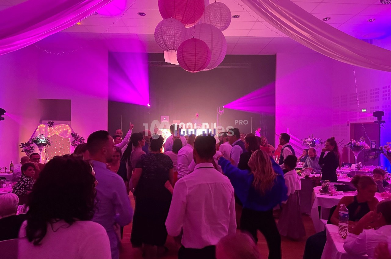 Groupe de personnes dansant dans une salle décorée avec des lanternes suspendues et éclairée par des lumières colorées.