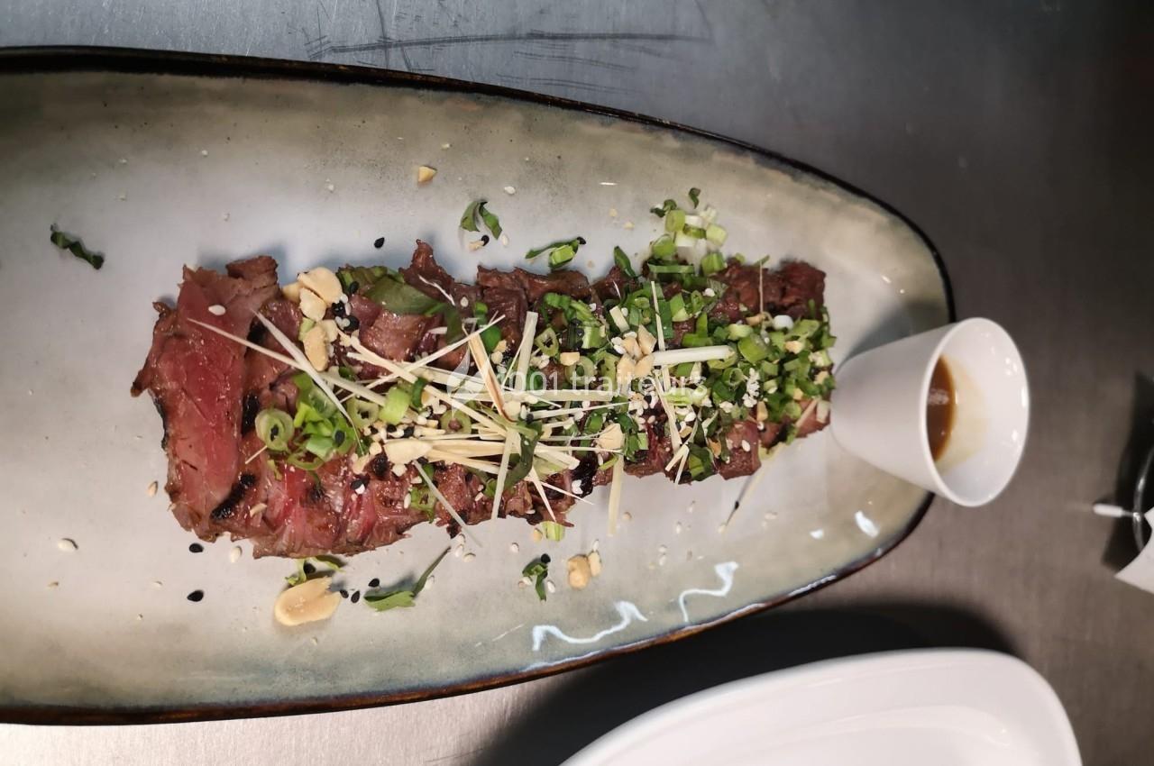 Tranche de viande grillée garnie de ciboulette, cacahuètes et graines, servie avec une sauce à part.