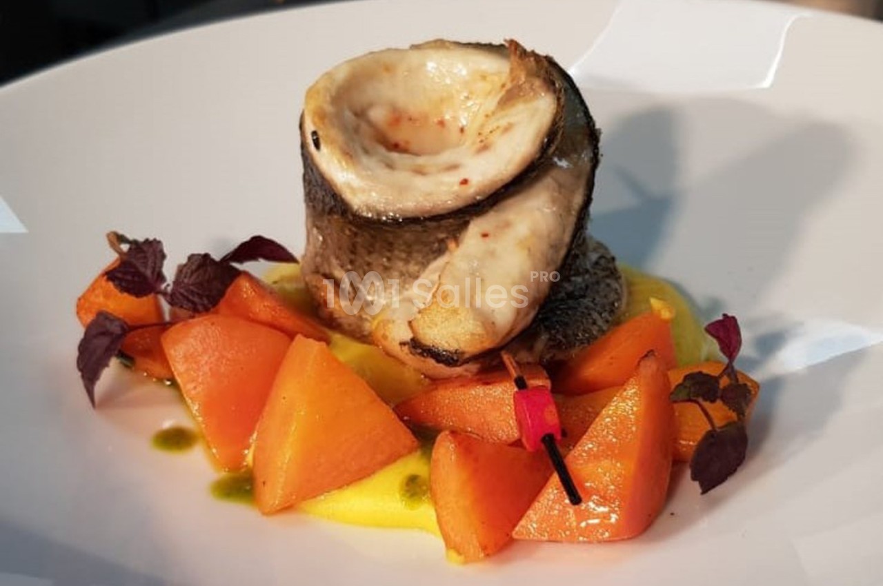 Filet de poisson roulé sur purée jaune, accompagné de morceaux de carottes et de feuilles décoratives.
