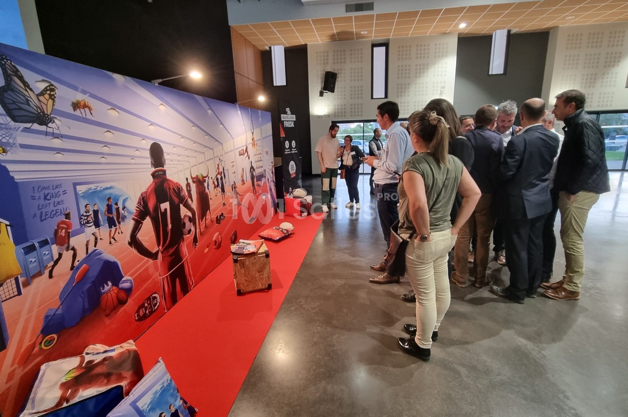 Un groupe de personnes observe une fresque colorée représentant des scènes sportives dans un espace intérieur.