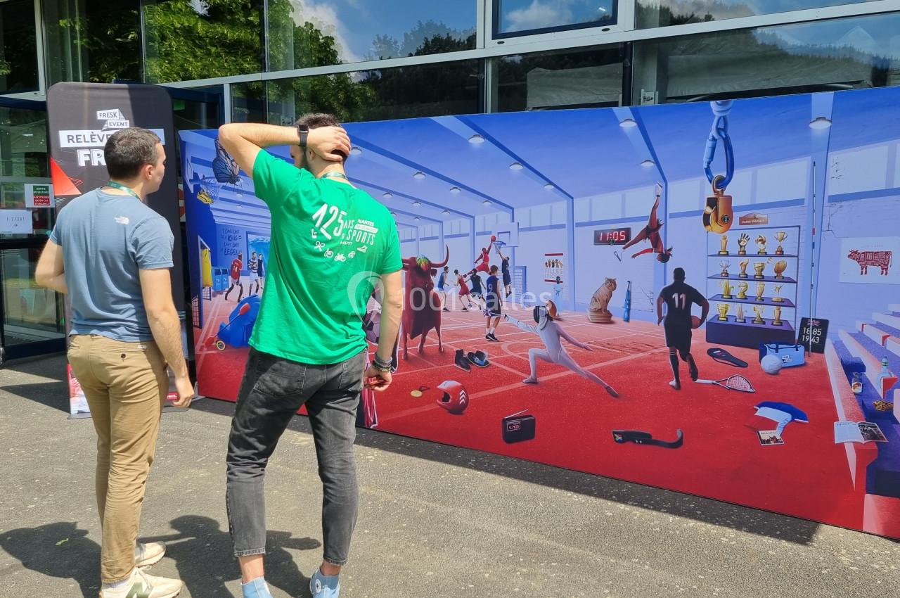 Deux hommes observent une fresque colorée représentant une salle de sport avec diverses activités et personnages.