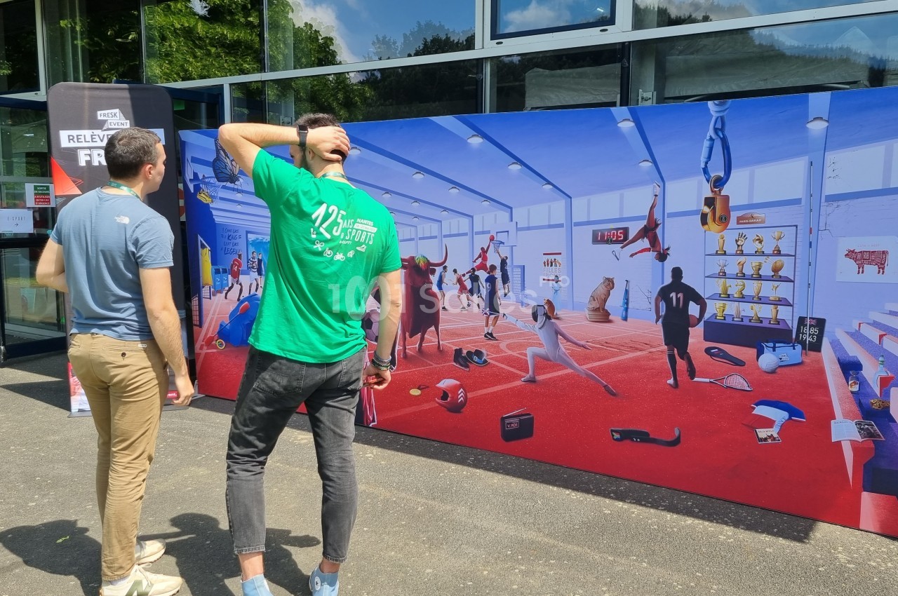Deux hommes observent une fresque colorée représentant une salle de sport avec diverses activités et personnages.