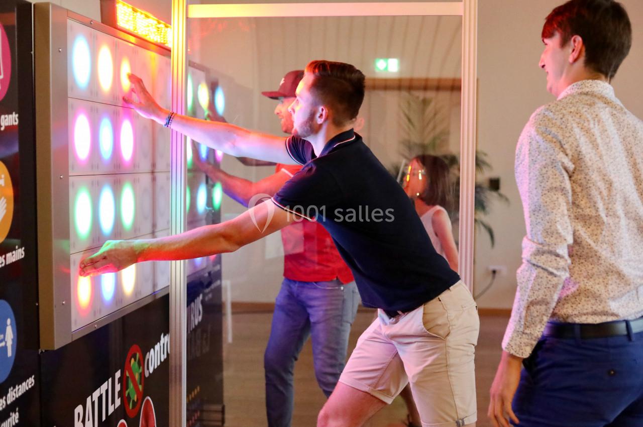 Deux personnes jouent à un jeu interactif lumineux, touchant des cibles colorées sur un panneau vertical.
