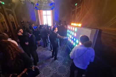 Personnes rassemblées dans une salle élégante, certaines interagissant avec un mur lumineux coloré.