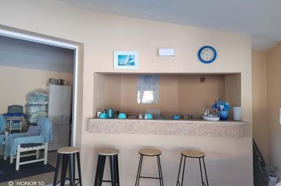 Terrasse avec table et chaises blanches sous une pergola, entourée de plantes et arbres dans un jardin ensoleillé.