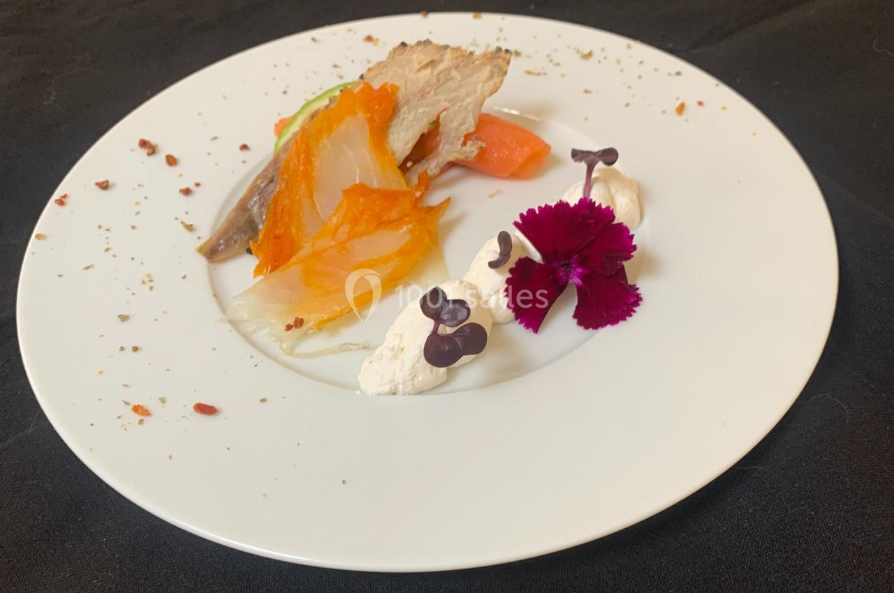 Assiette gastronomique avec légumes colorés, crème, fleurs comestibles et morceau de viande, présentée sur une nappe noire.