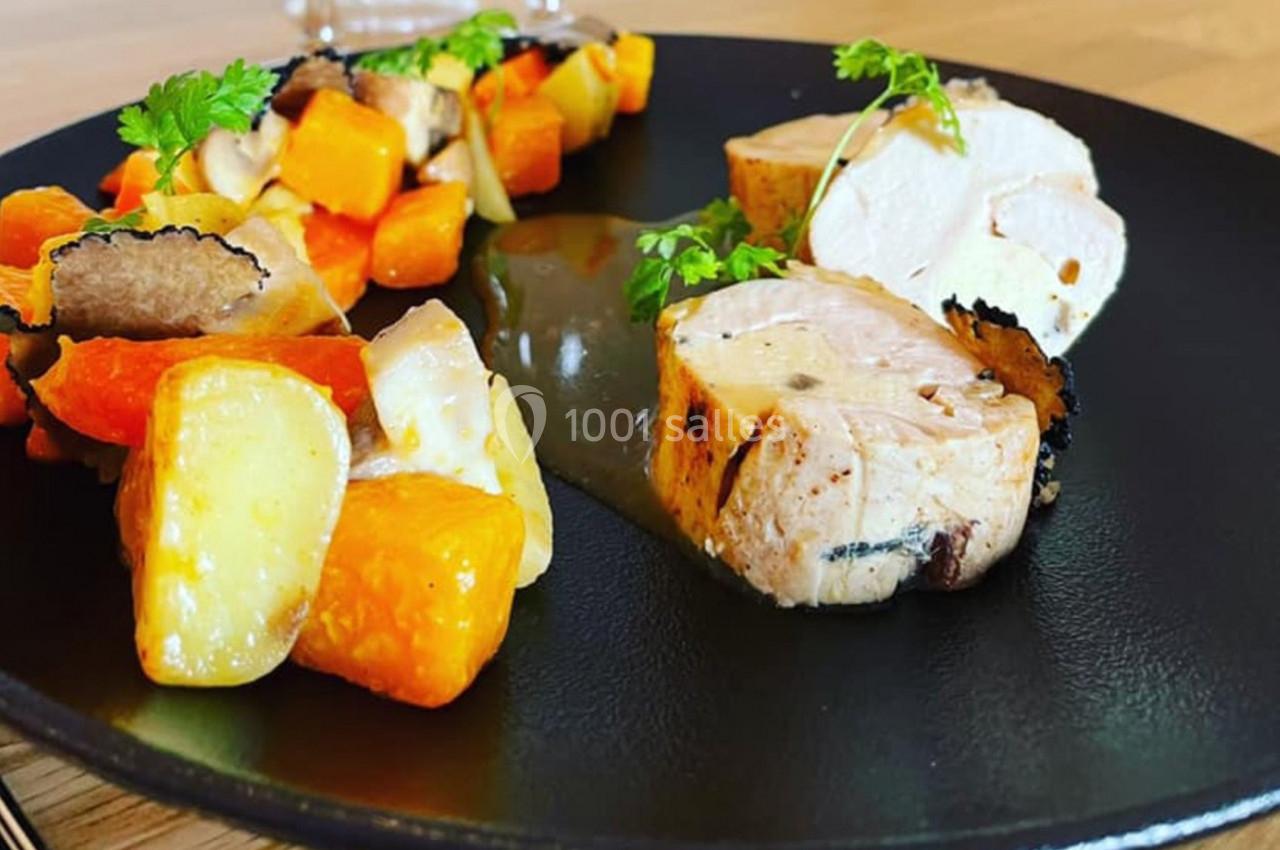 Assiette garnie de volaille tranchée, légumes rôtis et sauce, présentée sur une assiette noire.
