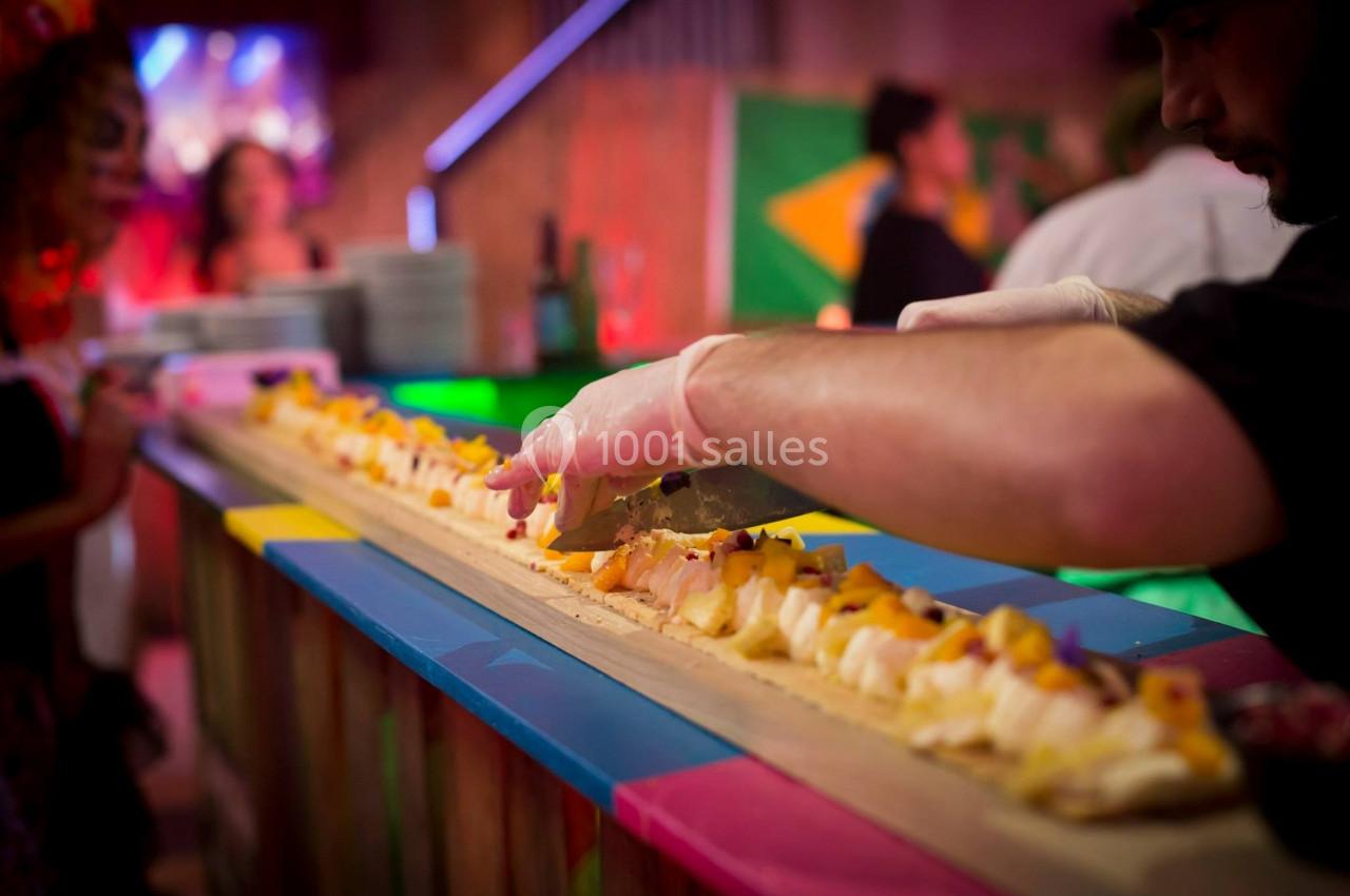 Un chef découpe un long plateau de sushis garnis de fruits dans un environnement festif et coloré.