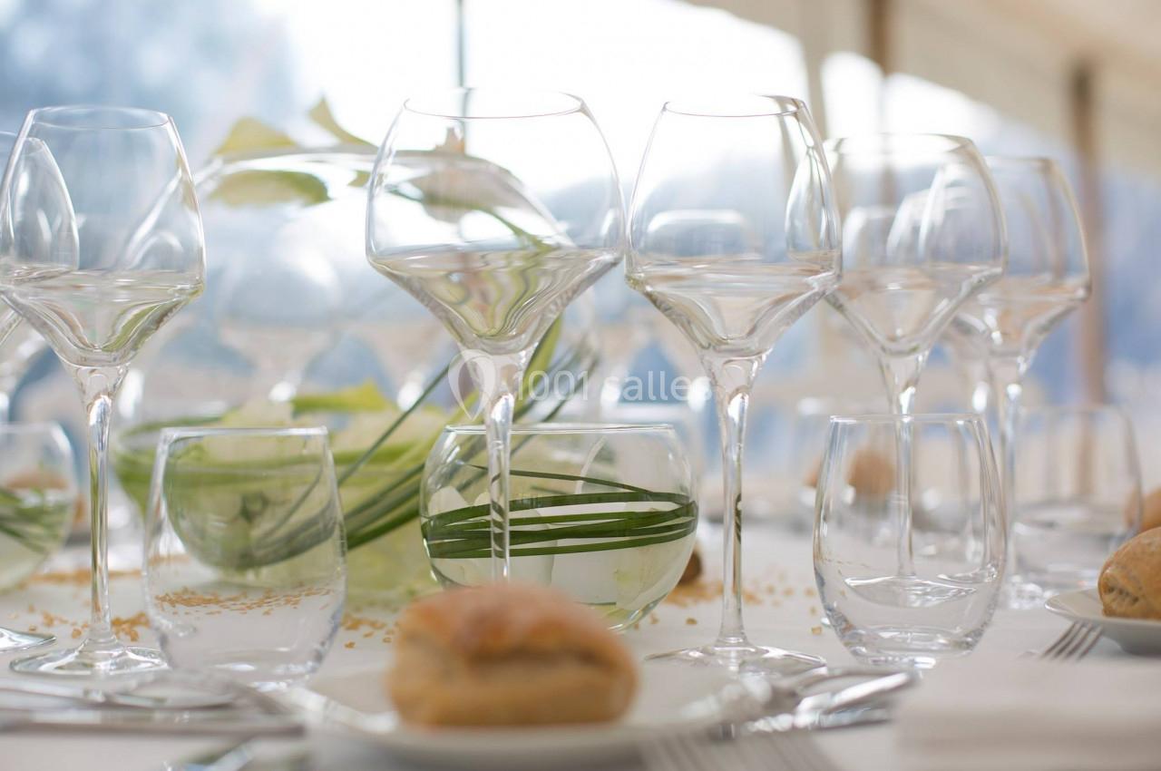 Table dressée avec des verres à vin et à eau, des assiettes, un pain individuel et une décoration végétale.
