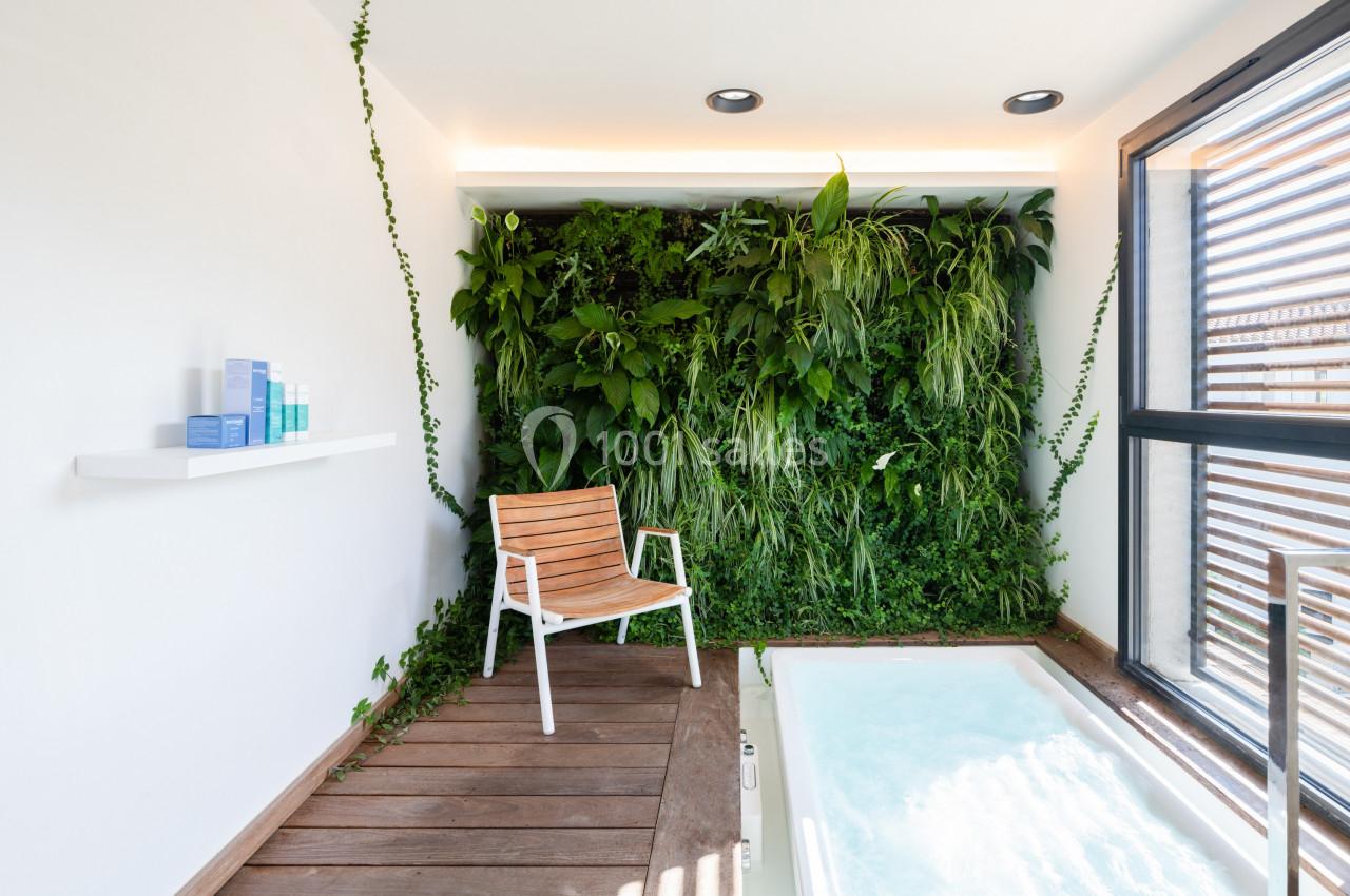 Mur végétal avec chaise en bois, terrasse en bois et jacuzzi dans un espace lumineux avec lumière naturelle.