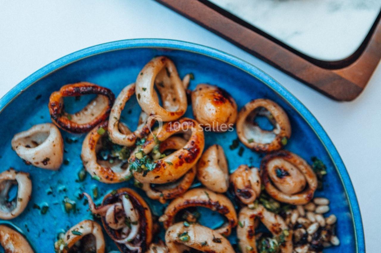 Anneaux de calamars grillés avec herbes et pignons de pin, servis dans une assiette bleue.