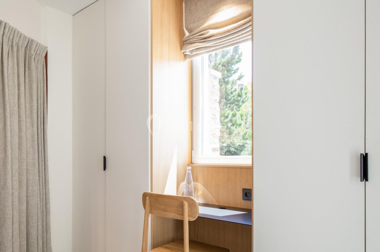 Coin bureau minimaliste avec une chaise en bois, un bureau intégré près d'une fenêtre et des rangements encastrés.