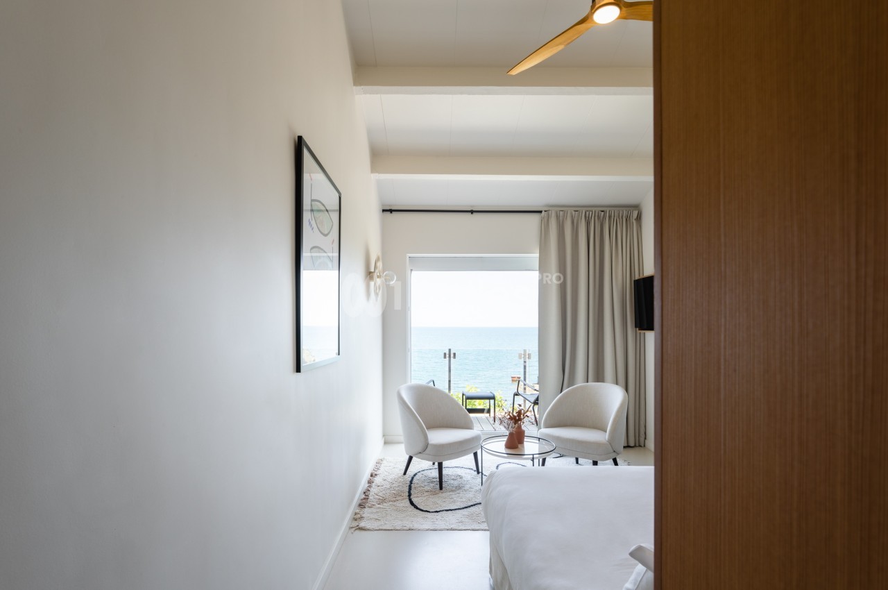Chambre lumineuse avec vue sur la mer, décorée de fauteuils blancs, table basse et rideaux clairs.