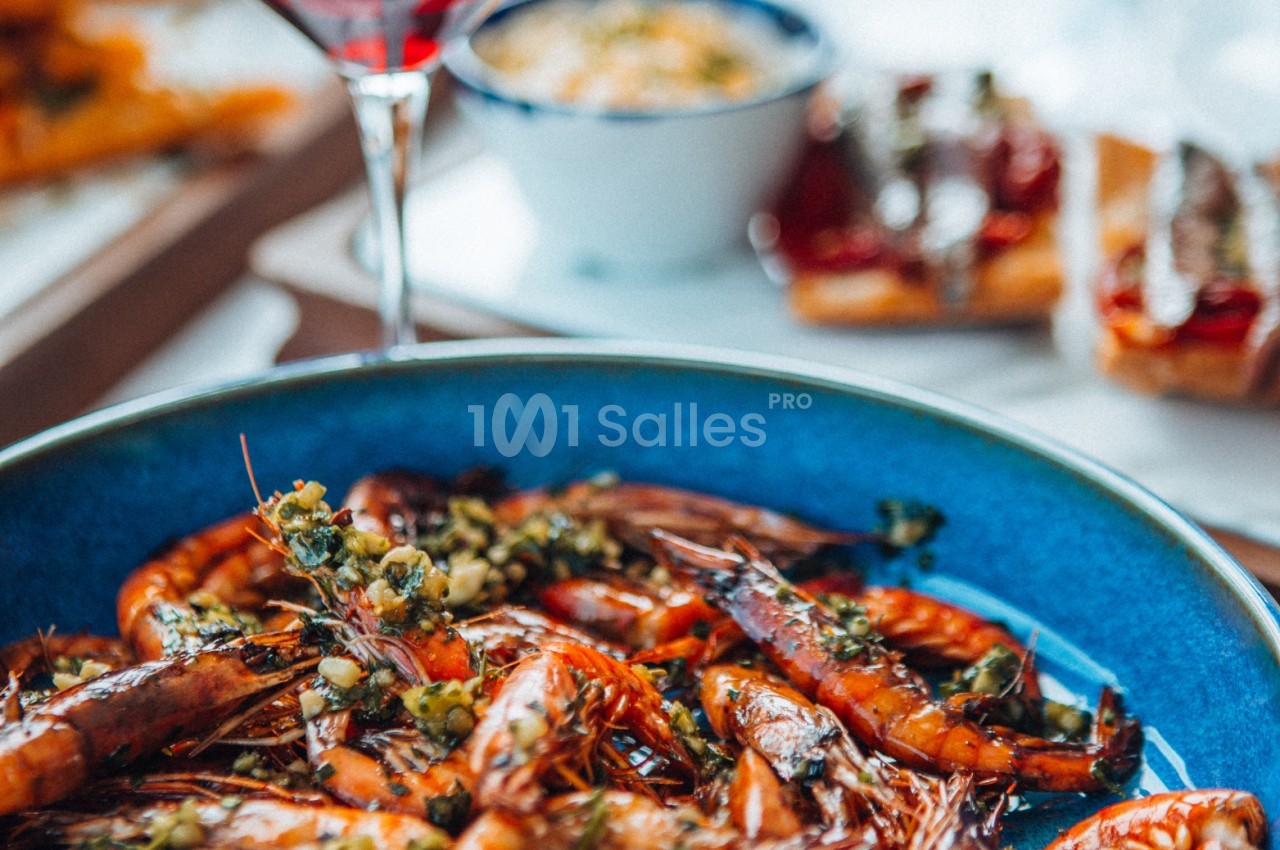 Crevettes grillées servies dans une assiette bleue avec des herbes, accompagnées de plats et d'un verre de vin rouge.
