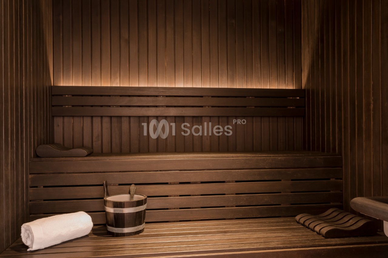 Bancs en bois dans un sauna avec un seau, une louche, une serviette blanche et un coussin disposés sur les surfaces.