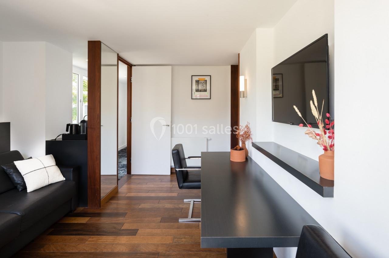 Salon moderne avec parquet, bureau noir, télévision murale, canapé noir et décoration minimaliste.