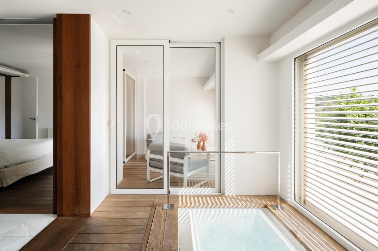 Salle lumineuse avec baie vitrée, fauteuils sur un balcon, parquet en bois et petite piscine intérieure.