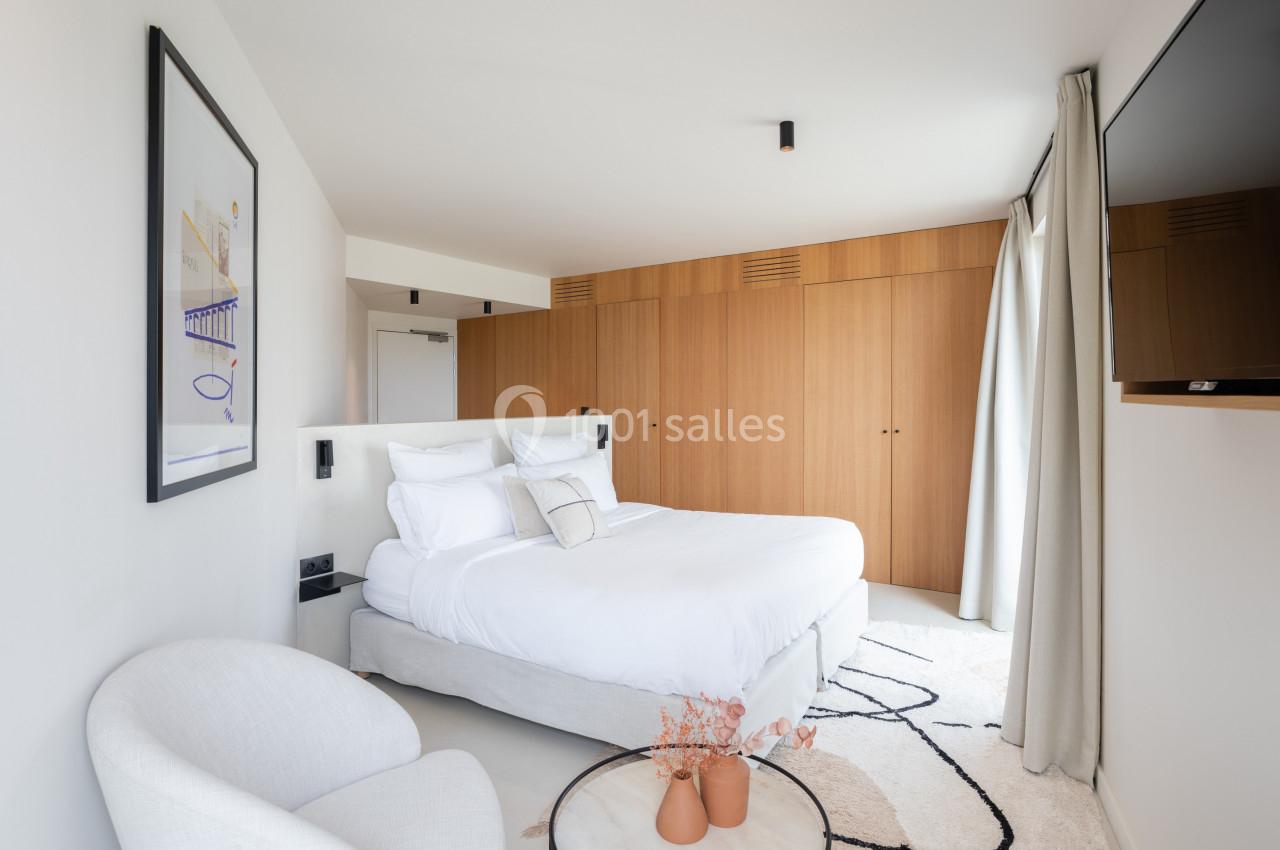Chambre lumineuse avec lit double, fauteuil, table basse décorée et grand placard en bois clair.