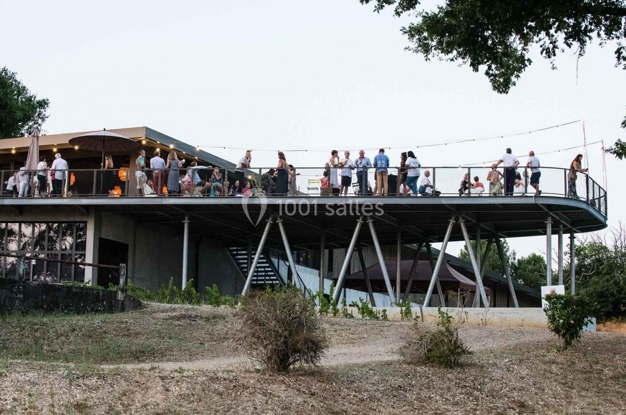 Terrasse surélevée avec des personnes réunies, entourée de végétation et éclairée en soirée.