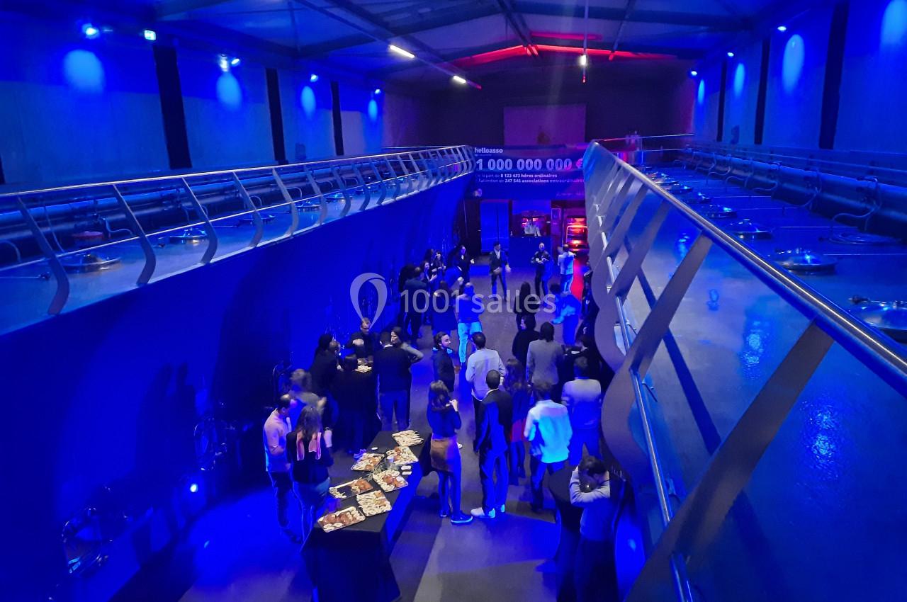 Salle moderne éclairée de lumières bleues, avec des groupes de personnes discutant près de tables et d'expositions.