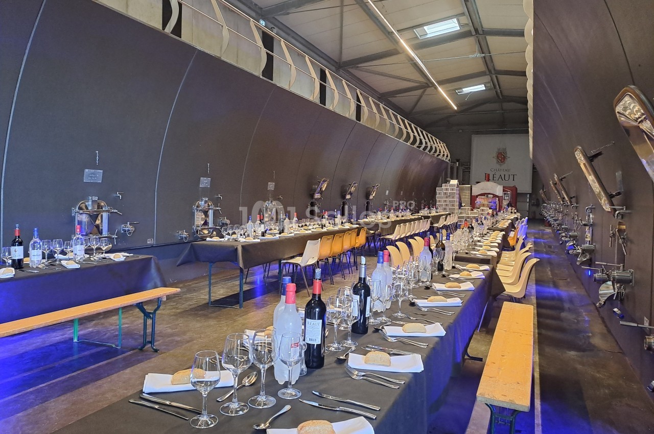Salle de réception aménagée dans une cave avec de longues tables dressées, décor sobre et éclairage tamisé.