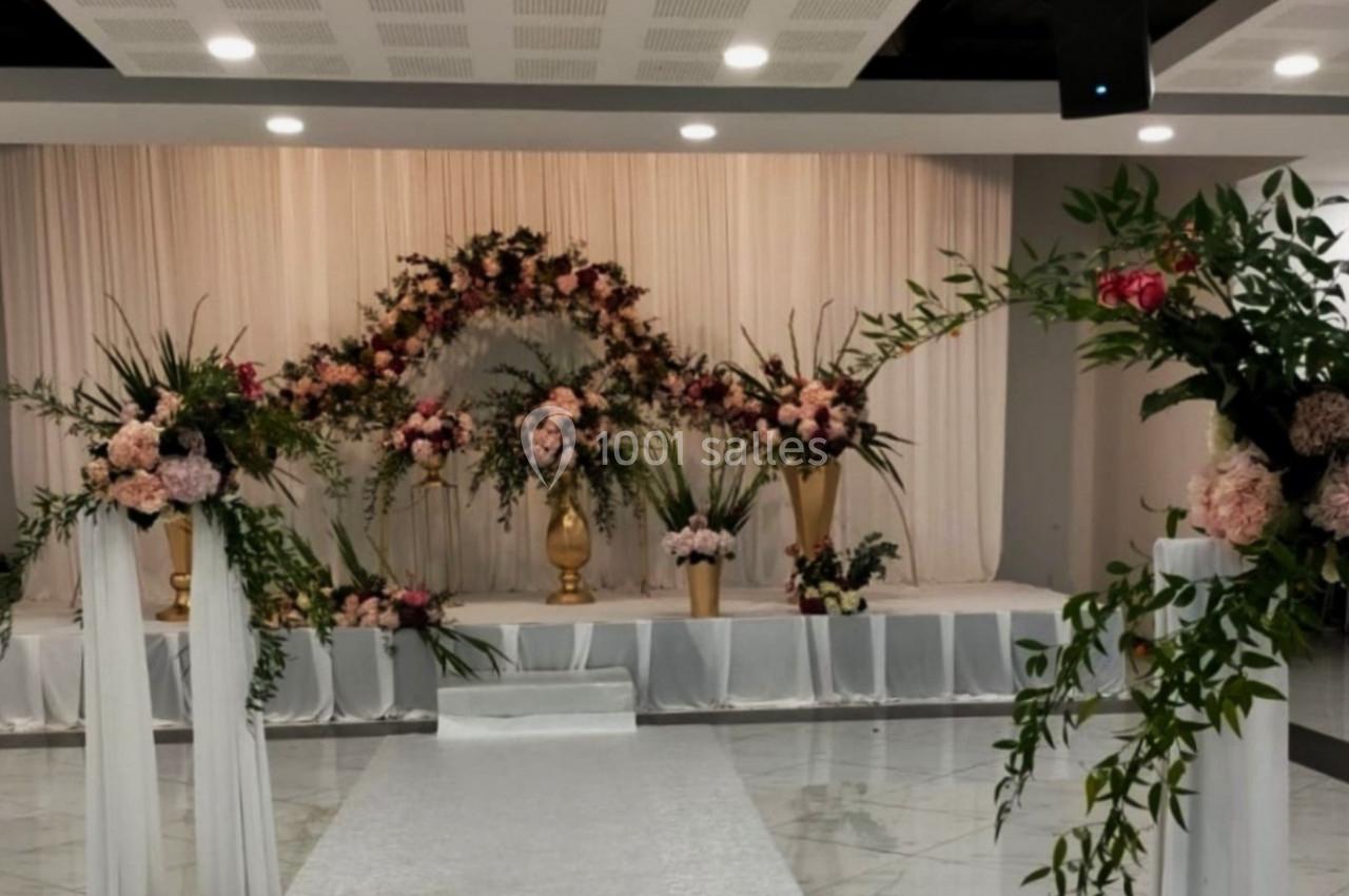Décor floral élégant avec des arches de fleurs roses et blanches, disposé sur une scène dans une salle de réception.