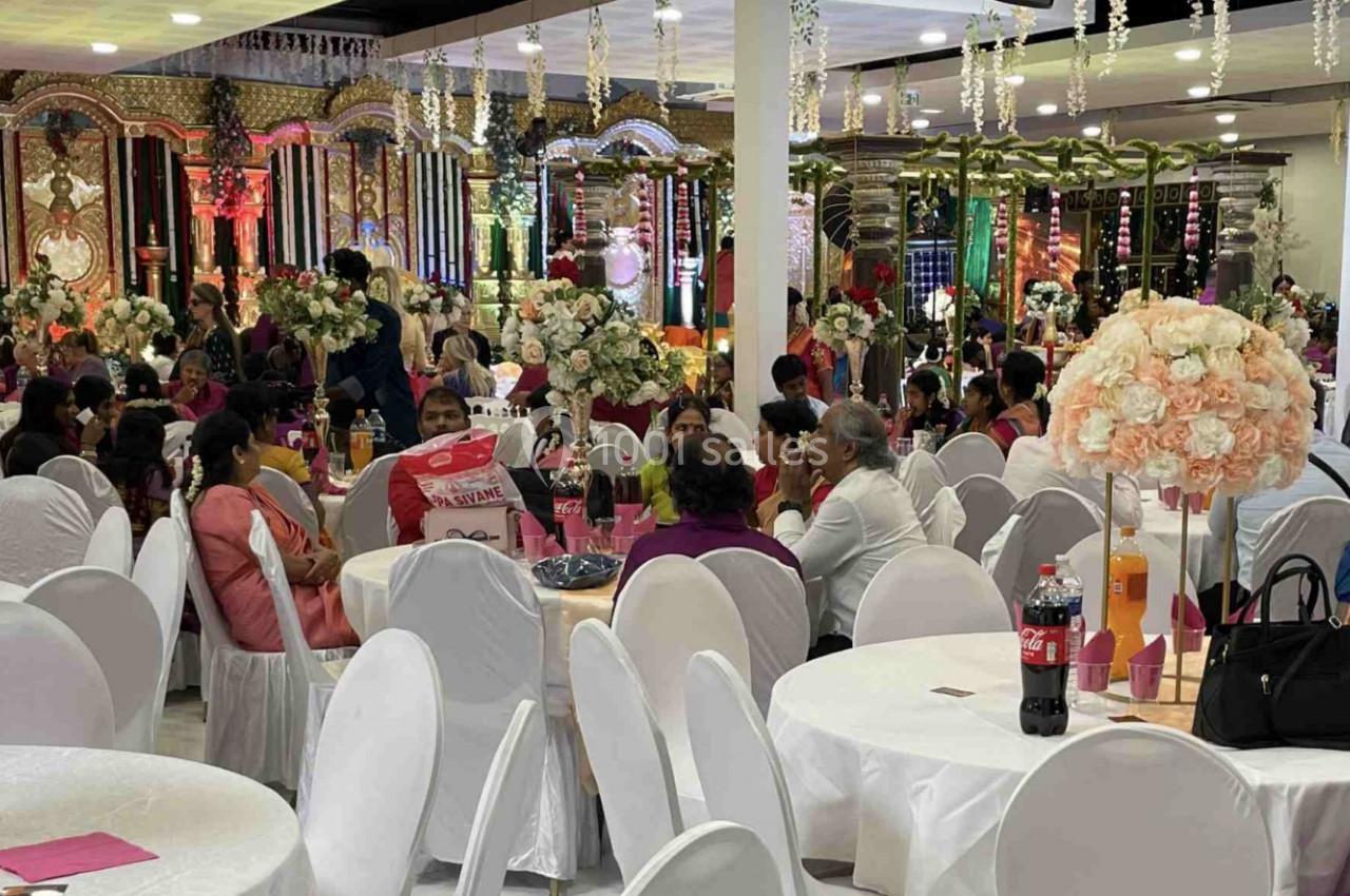 Salle de réception décorée avec des tables rondes, des chaises blanches et des invités assis lors d'un événement festif.
