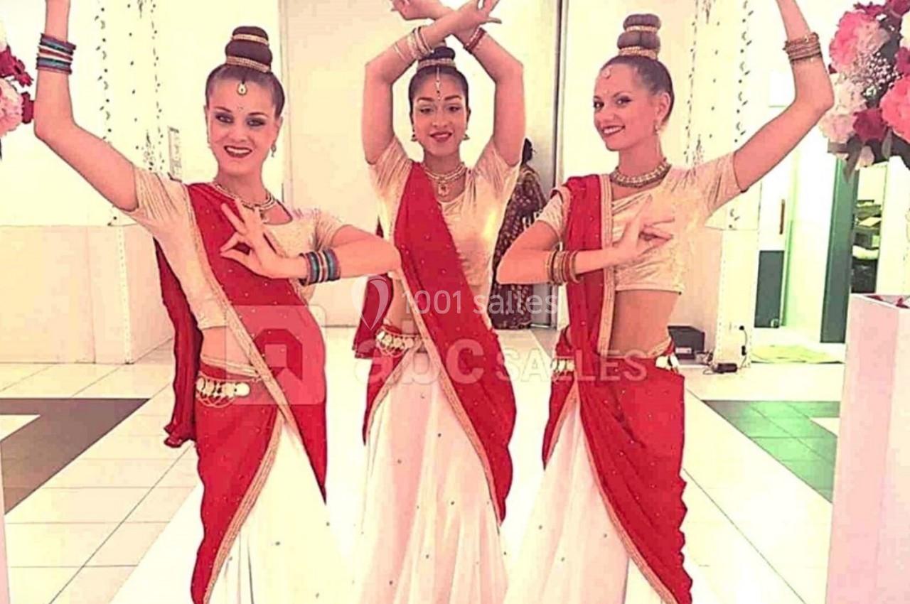Trois femmes en tenue traditionnelle indienne exécutant une danse, entourées de colonnes décorées de fleurs.