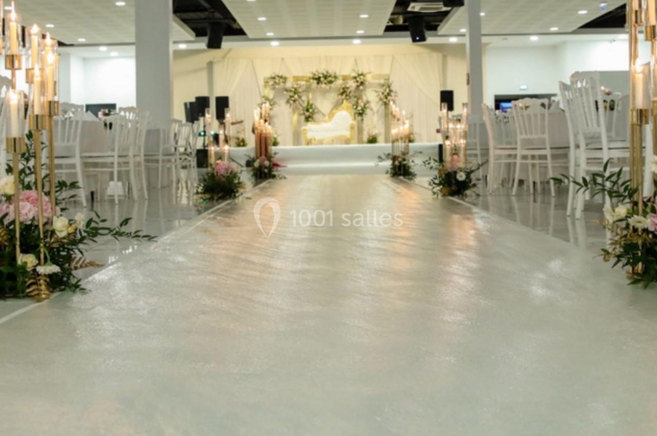 Allée centrale décorée de fleurs et bougies menant à une scène ornée pour un événement ou une cérémonie.