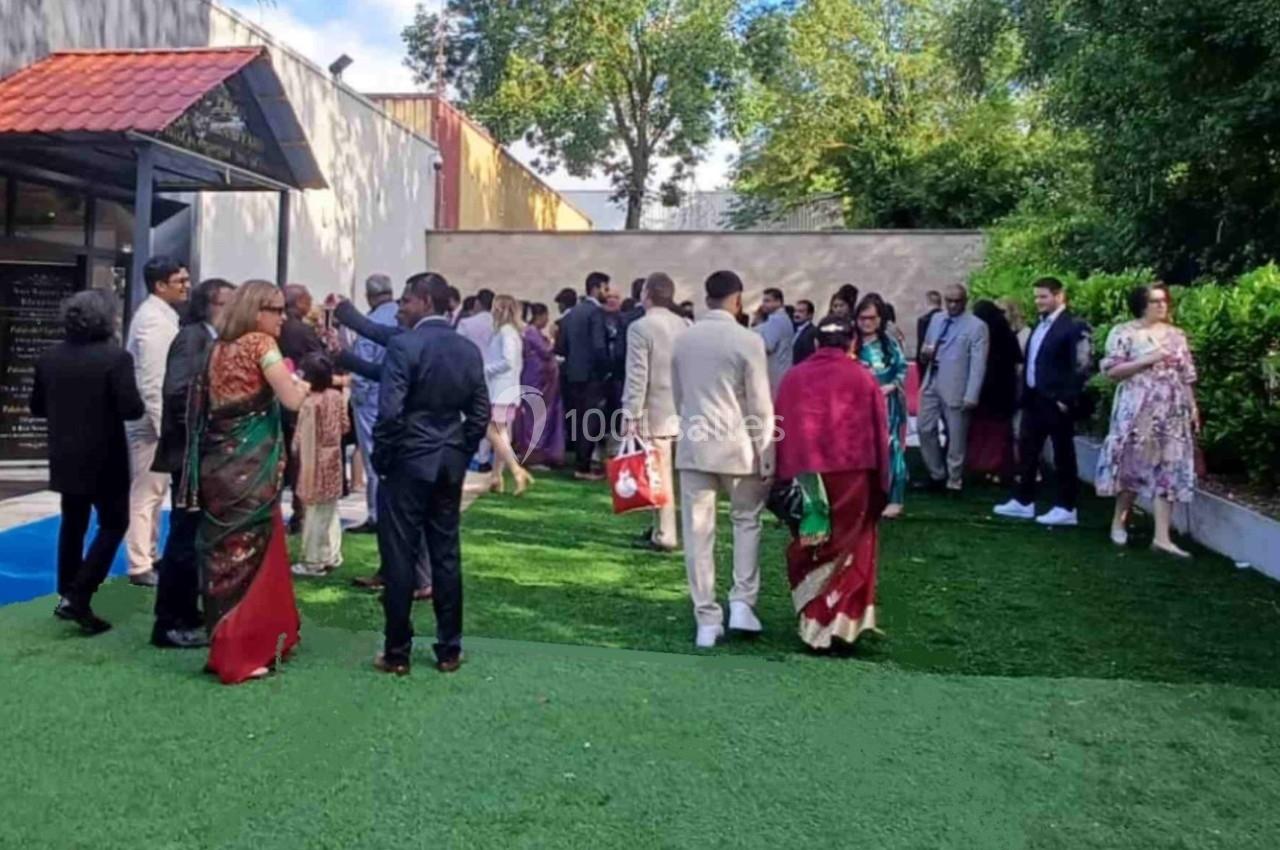 Un groupe de personnes en tenue habillée discute dans un jardin extérieur près d'un bâtiment moderne.