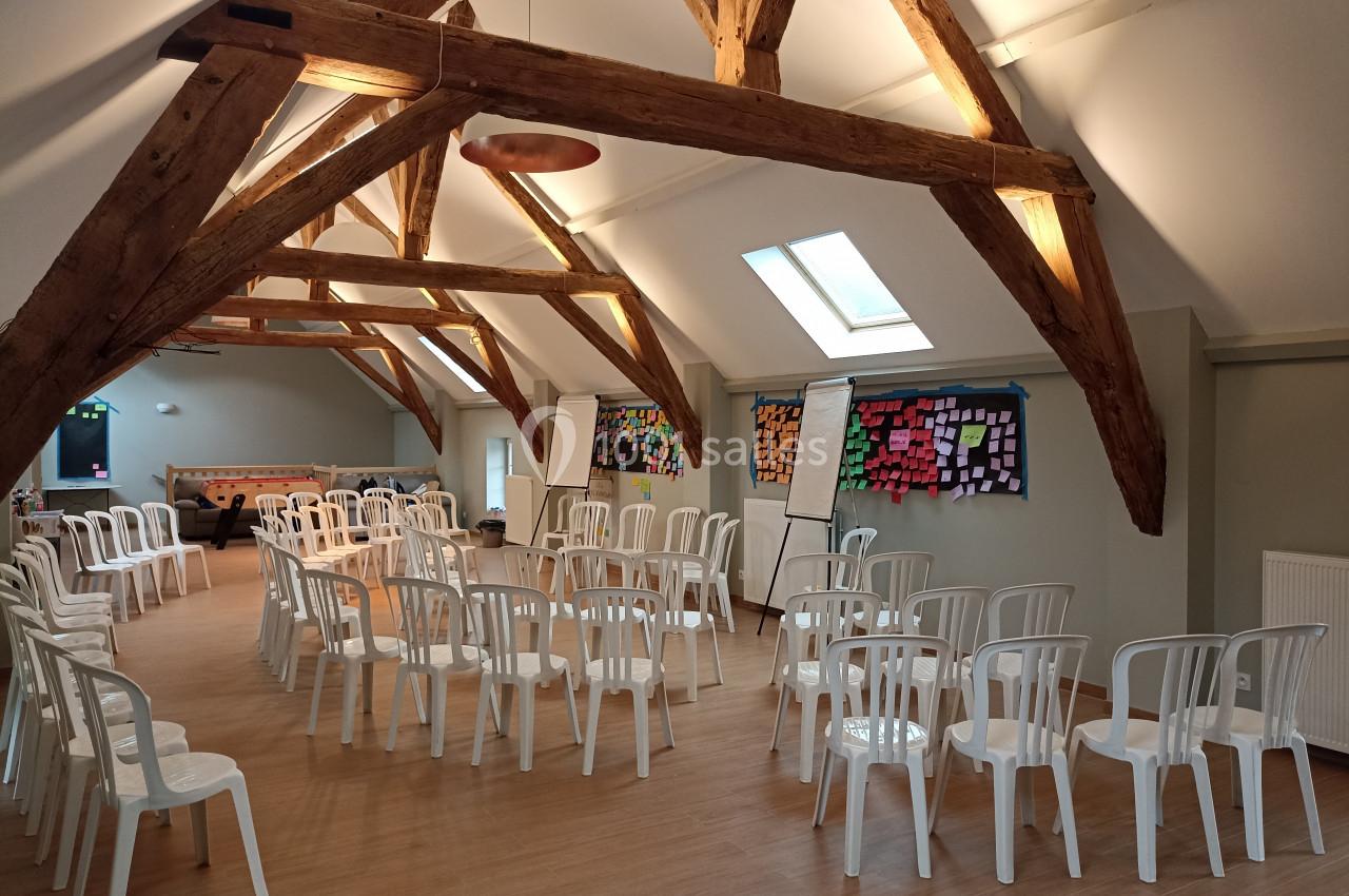 Salle lumineuse avec charpente en bois, chaises blanches disposées en cercle et murs couverts de post-it colorés.