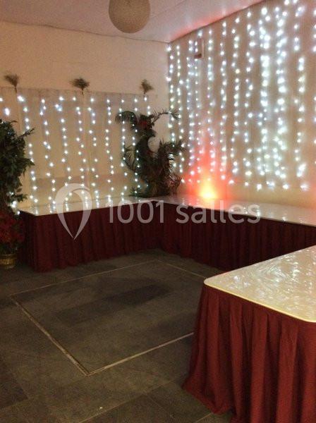 Salle décorée avec des guirlandes lumineuses blanches, tables recouvertes de nappes blanches et jupes rouges.