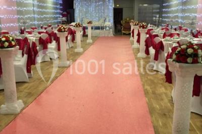 Salle décorée pour un événement avec tables rondes, nappes blanches, chaises ornées de nœuds argentés et dorés, éclairage…