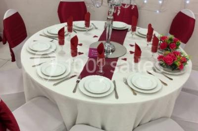 Salle décorée pour un événement avec tables rondes, nappes blanches, chaises ornées de nœuds argentés et dorés, éclairage…