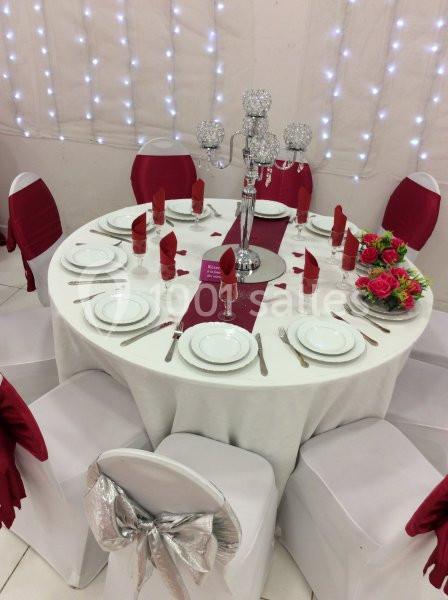 Table ronde élégamment dressée avec nappes blanches, serviettes rouges, centre de table argenté et décor floral.