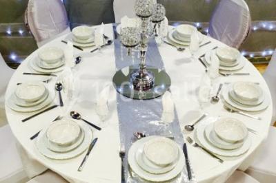Salle décorée pour un événement avec tables rondes, nappes blanches, chaises ornées de nœuds argentés et dorés, éclairage…