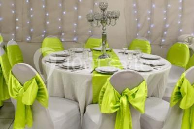 Salle décorée pour un événement avec tables rondes, nappes blanches, chaises ornées de nœuds argentés et dorés, éclairage…