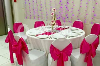 Salle décorée pour un événement avec tables rondes, nappes blanches, chaises ornées de nœuds argentés et dorés, éclairage…