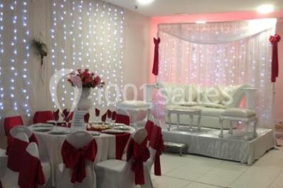 Salle décorée pour un événement avec tables rondes, nappes blanches, chaises ornées de nœuds argentés et dorés, éclairage…