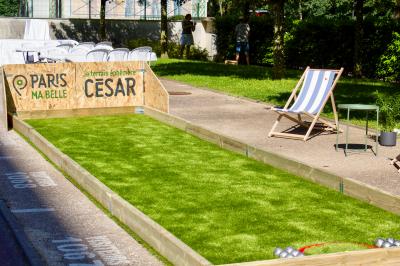 Terrain de pétanque en plein air avec chaises pliantes, parasol et espace ombragé entouré de verdure.
