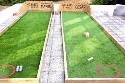Terrain de pétanque en plein air avec chaises pliantes, parasol et espace ombragé entouré de verdure.