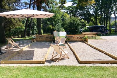 Terrain de pétanque en plein air avec chaises pliantes, parasol et espace ombragé entouré de verdure.