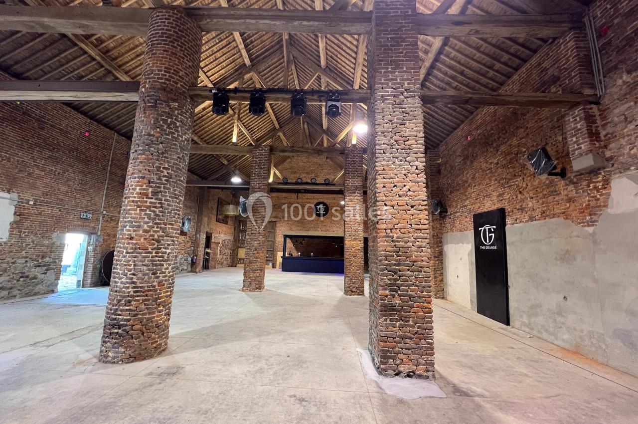 Intérieur d'une grande salle en briques avec poutres apparentes, colonnes en briques et espace ouvert.