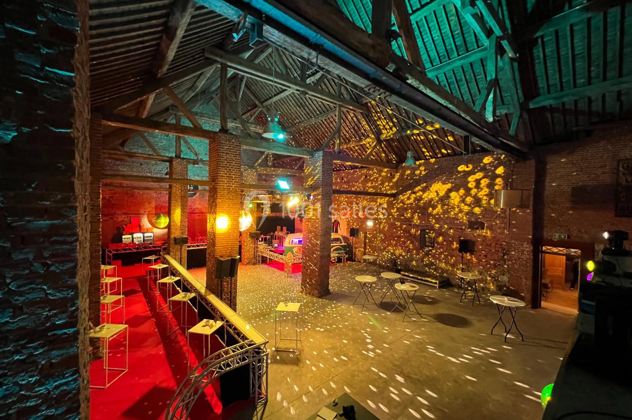 Salle en briques avec poutres apparentes, éclairée par des lumières colorées et des reflets de boule disco.