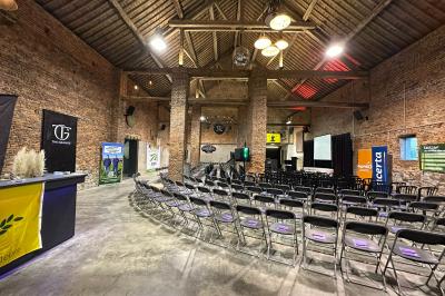 Parking en gravier entouré d'arbres et de bâtiments en briques sous un ciel partiellement nuageux.