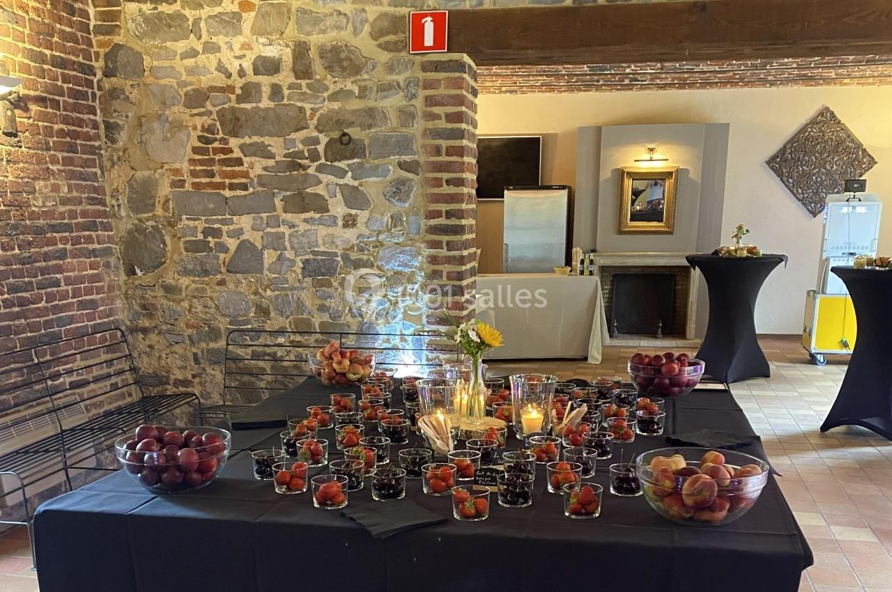 Table décorée avec des bougies, des fruits rouges et des pêches, dans une salle aux murs en pierre et briques apparentes.