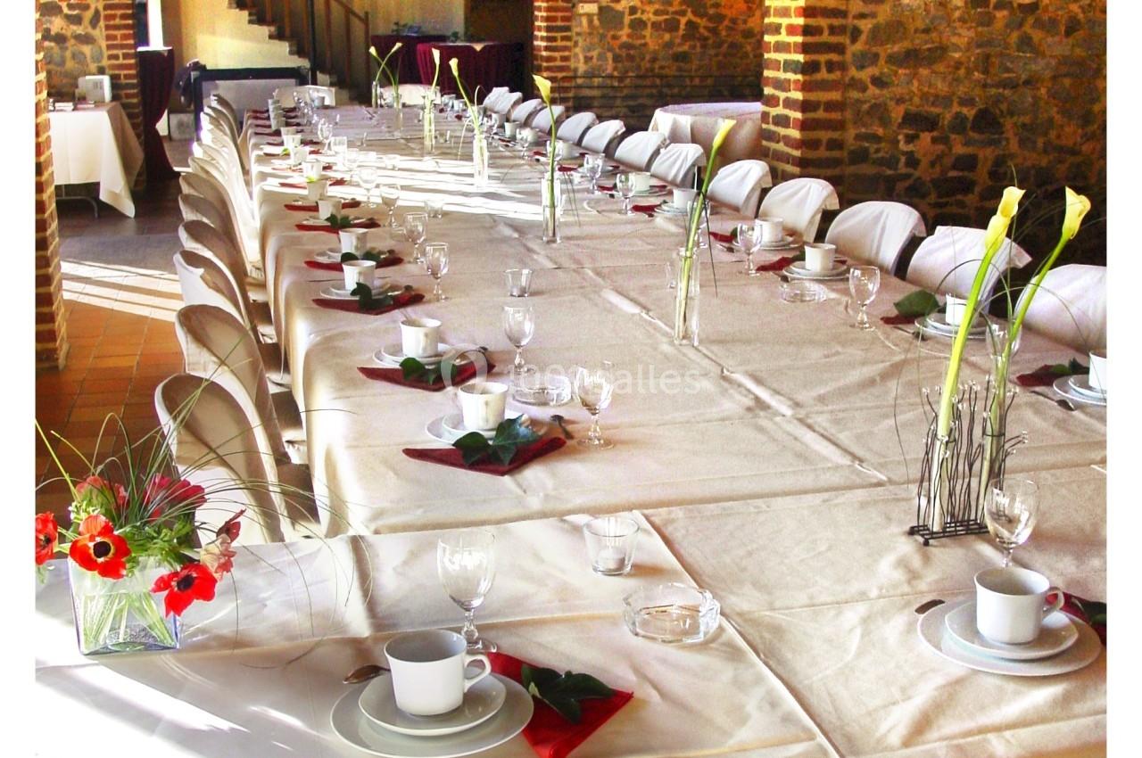 Grande table dressée pour un repas, avec nappes blanches, vaisselle, serviettes rouges et décorations florales.